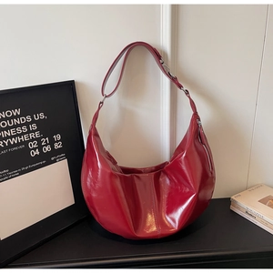 Detail of dark red hobo bag showing glossy patent leather texture and pleated bottom design