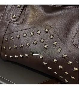 Close-up detail of brown litchi leather texture and square metal rivets on the tote bag