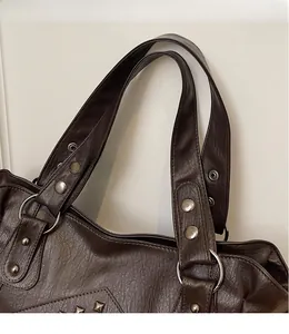 Detail of wide strap connection with silver rivets on dark brown leather tote bag