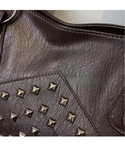 Close-up of textured brown leather tote bag featuring polished square metal rivets