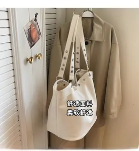 Detail of a cream tote bag with silver metal eyelet straps hung in a cozy indoor setting