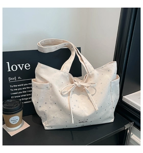 Detail of a beige canvas tote bag with silver star prints and a drawstring bow decoration