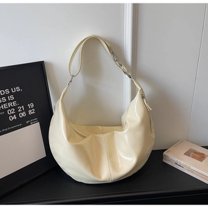 Detail view of glossy cream croissant bag featuring silver metallic buckle and zipper