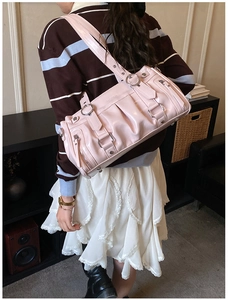 Sac fourre-tout en cuir verni rose avec plis et rivets argentés porté par un mannequin