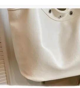 Close-up of white pebble grain leather tote with silver metal grommets and rivets detail