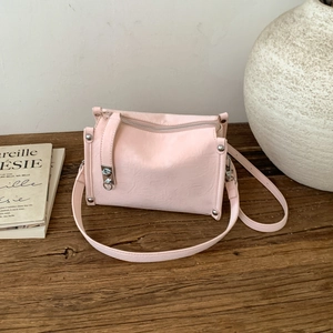 Detail of pink pillow bag with silver rivets and metal clasp on dark wooden desk