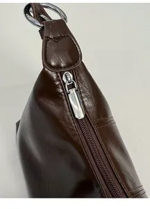 Detail view of the silver metal zipper and smooth leather texture on a dark brown bag