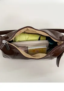 Detail view of spacious dark brown patent leather shoulder bag holding daily essentials