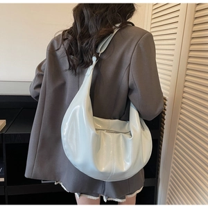 Detail showing high-gloss light blue crescent bag worn on shoulder in soft lighting