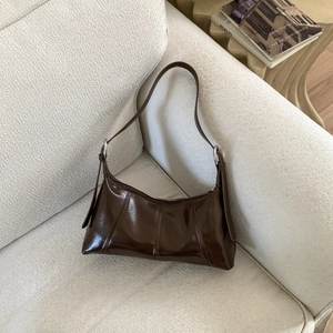 Detail of dark brown glossy hobo bag with stitching on cream textured sofa