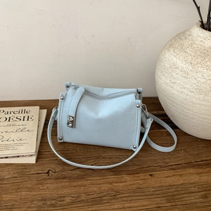 Detail of light blue pillow bag with silver studs and faux leather texture on wood surface