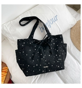 Detailed macro of black canvas tote bag featuring white stars and a handmade metal plate