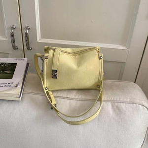 Detail of pale yellow crossbody bag with wrinkled texture and silver studs on a sofa
