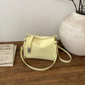Minimalist light yellow pillow shoulder bag with silver rivets on a wooden surface
