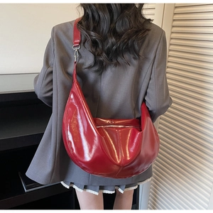 Detailed view of large bright red patent leather crescent bag worn on model shoulder
