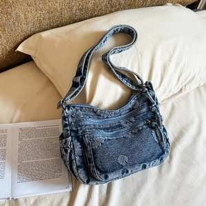 Detail of blue denim shoulder bag featuring floral embroidery and functional multi-pockets