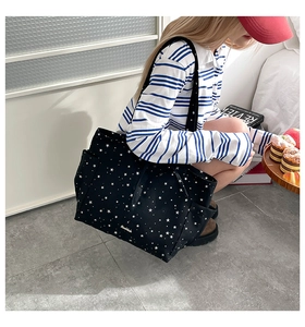 Detail of black star print tote bag featuring a gold handmade metal plaque and side pocket