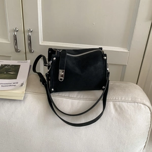 Detail view of black matte leather pillow bag with silver buckle on a white sofa