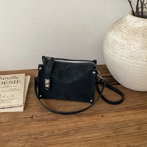 Detail of black suede pillow bag with silver studs and premium metal zipper on a desk