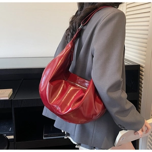 Detail of red glossy patent leather hobo bag with vintage pleated texture and wide strap