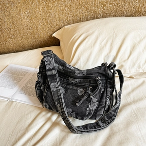 Detailed view of black denim shoulder bag with white floral patterns and zipper pockets