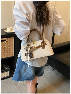 Sac bandoulière en toile beige et cuir marron porté par un mannequin en intérieur doux