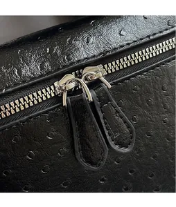 Close-up of black ostrich pattern leather bag with dual silver zippers and long pulls