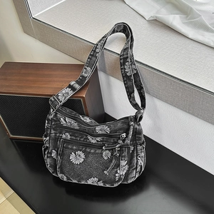 Detail view of denim crossbody bag featuring white daisy prints and multi-zippered pockets
