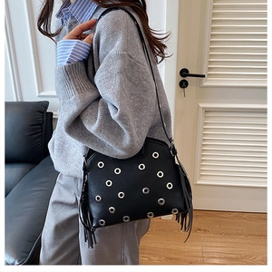 Dettaglio della borsa in pelle nera con occhielli argentati e lunghe frange laterali