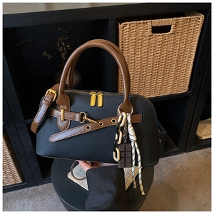 Détail du sac bowling en cuir noir avec poignées marron et pendentifs de mode