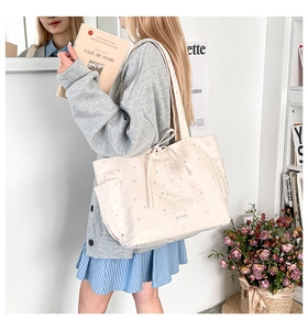 Detail of off-white tote bag with silver star patterns, side pocket, and drawstring