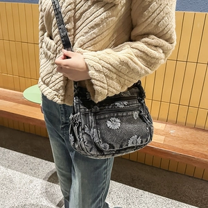 Detail of grey denim crossbody bag featuring white daisy prints and multi-zipper pockets