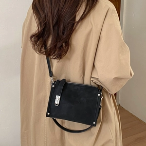 Detailed view of black textured crossbody bag featuring silver rivets on a khaki trench coat