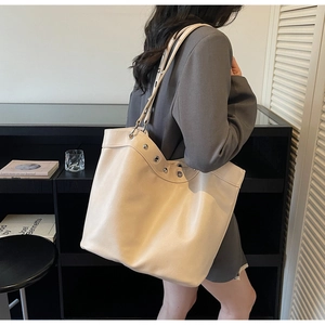 Detail view of cream oversized leather tote bag with silver eyelets on a shoulder strap