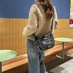 Detail of grey denim crossbody bag with white daisy embroidery on minimalist background