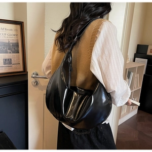 Detailed view of large black patent leather hobo bag worn as a shoulder bag