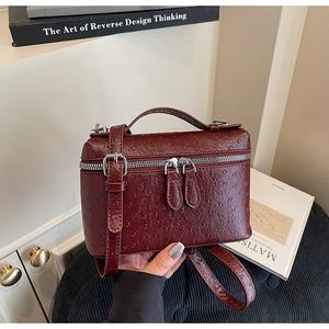 Detail view of burgundy ostrich embossed leather handbag with silver dual zipper closure