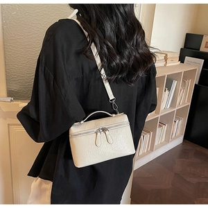 Detail of a cream ostrich-pattern square bag worn as a crossbody on a black shirt