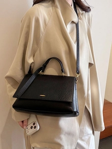 Sac fourre-tout vintage en cuir noir avec fermoir doré sur un trench-coat beige