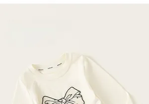Détail d'un t-shirt crème à manches longues avec un grand nœud décoratif et col rond doux
