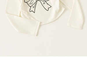 Détail d'un t-shirt crème à manches longues avec imprimé nœud noir sur coton doux