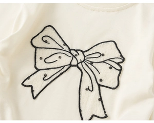 Détail du t-shirt crème pour fille avec un grand nœud en dentelle blanche à pois noirs