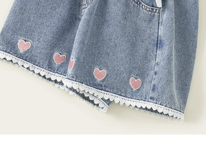 Detailed view of girl's blue denim shorts featuring pink heart embroidery and white lace trim