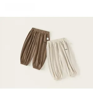 Détail de joggeurs enfants montrant les textures en coton lin marron et blanc cassé et broderie