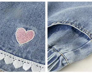 Detail of girls denim shorts featuring pink heart embroidery and white lace trim with pockets