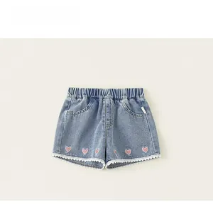 Detail of girl's denim shorts featuring pink heart embroidery and delicate white lace trim