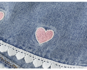Close-up of pink heart embroidery and white lace trim on blue denim girl's shorts