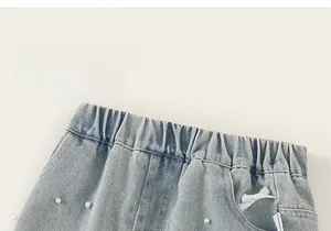 Dettaglio di pantaloncini di jeans chiari con vita elastica, perle e fiocchi in pizzo