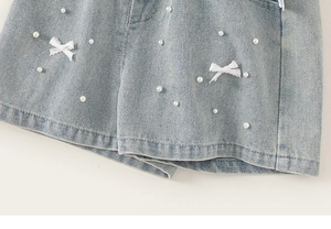 Dettaglio di perle bianche e fiocchi di pizzo su shorts in denim azzurro per bambine