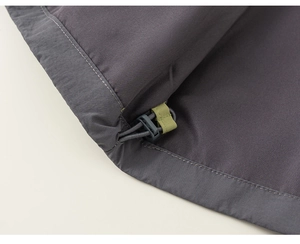 Detail des verstellbaren Saums mit grauem Kordelstopper und grünem Gurtband der Jacke